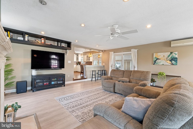 living area with wood finished floors, a textured ceiling, baseboards, and a wall mounted AC