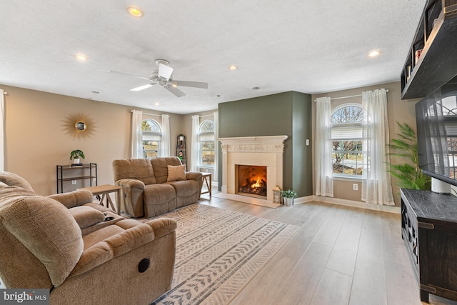 living room featuring a lit fireplace, a wealth of natural light, light wood-style flooring, and recessed lighting