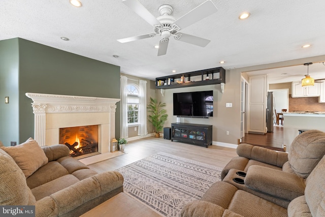 living room featuring a textured ceiling, recessed lighting, baseboards, light wood-style floors, and a lit fireplace