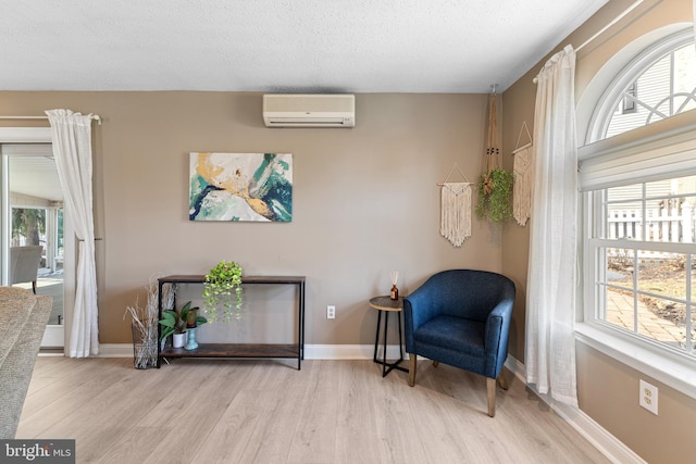 sitting room with wood finished floors, a healthy amount of sunlight, baseboards, and a wall mounted AC