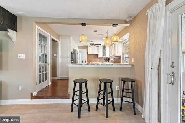 kitchen featuring baseboards, a breakfast bar, a peninsula, white cabinetry, and backsplash