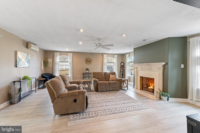 living room featuring a high end fireplace, a wall mounted air conditioner, light wood-style flooring, and baseboards