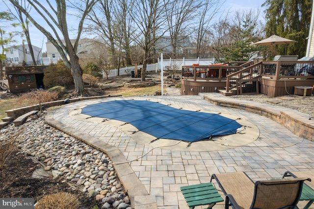 view of swimming pool featuring a patio, an outdoor structure, fence, a wooden deck, and a covered pool