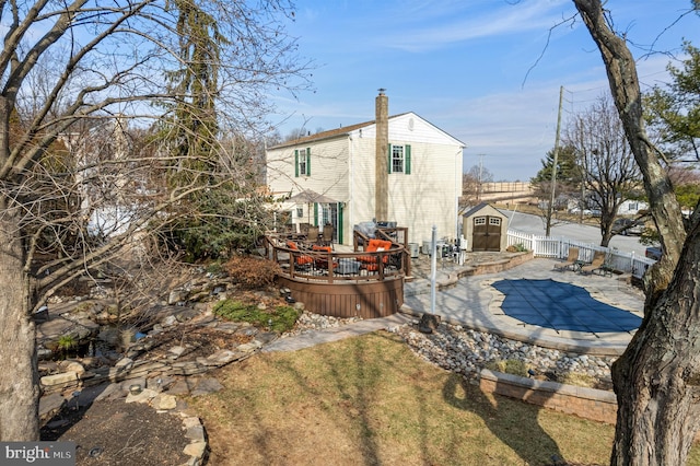 rear view of house with a chimney, a deck, a shed, a fenced backyard, and an outdoor structure