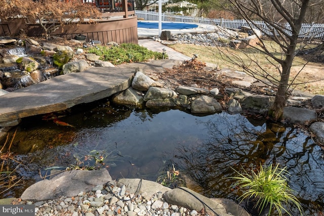 view of pool with a small pond and fence