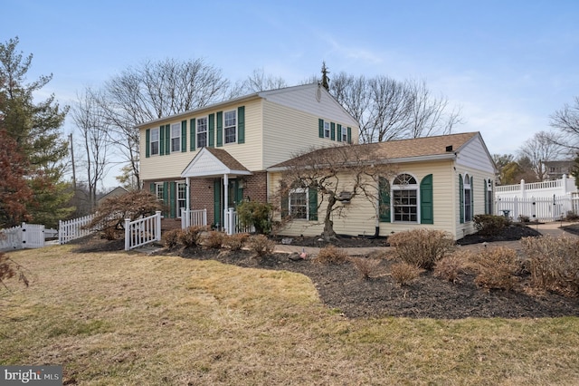 colonial house featuring brick siding, a gate, fence, and a front yard