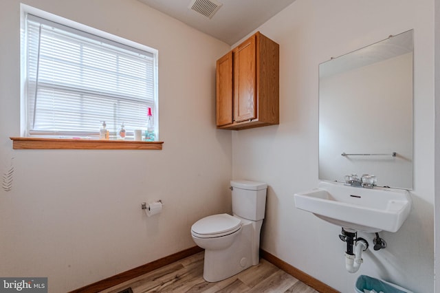 half bath featuring baseboards, visible vents, toilet, and wood finished floors