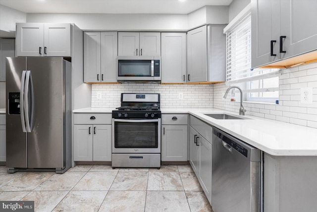 kitchen featuring tasteful backsplash, light countertops, gray cabinetry, appliances with stainless steel finishes, and a sink