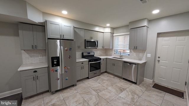 kitchen with light countertops, appliances with stainless steel finishes, a sink, and gray cabinetry