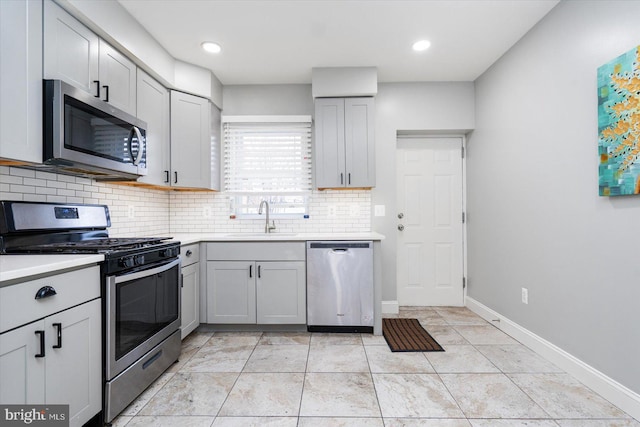 kitchen featuring stainless steel appliances, a sink, light countertops, gray cabinets, and backsplash