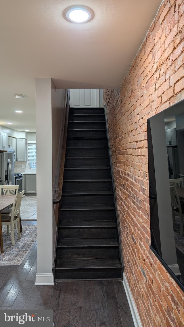 staircase featuring baseboards, brick wall, and wood finished floors