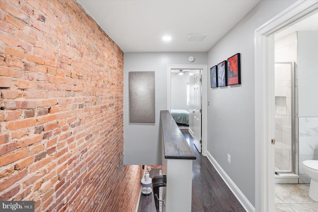 hall with dark wood-style floors, brick wall, visible vents, and baseboards