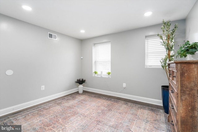 empty room with plenty of natural light, baseboards, visible vents, and wood finished floors