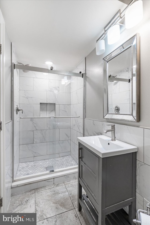 bathroom featuring marble finish floor, a shower stall, tile walls, and vanity