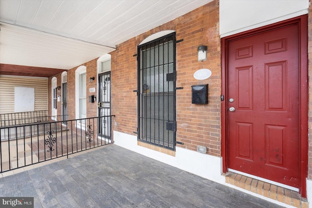 view of exterior entry featuring brick siding and a porch