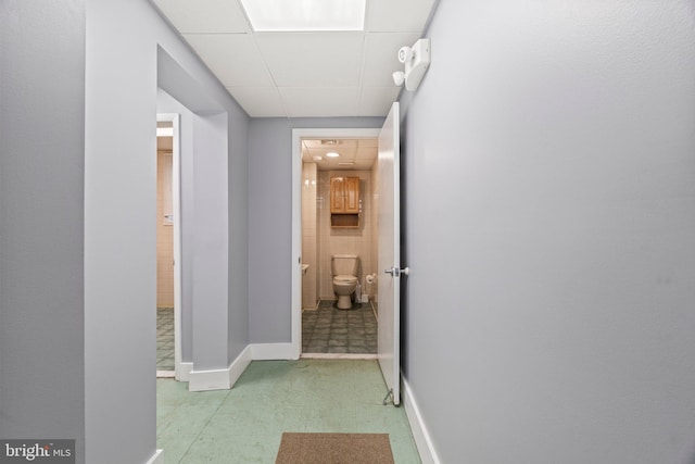 corridor with a paneled ceiling and baseboards