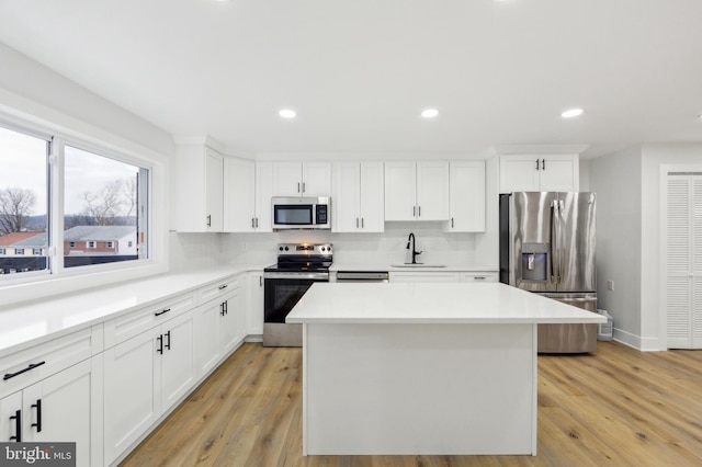 kitchen with a sink, stainless steel appliances, a kitchen island, and light countertops