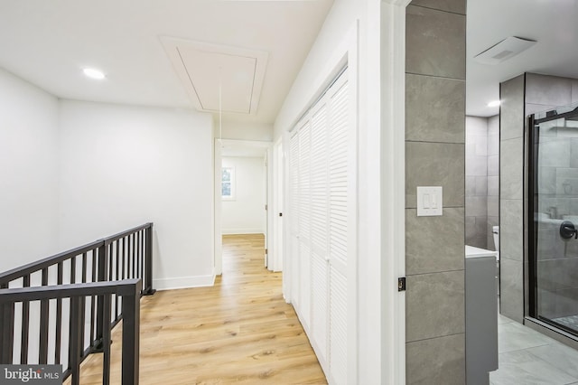 corridor featuring baseboards, attic access, and light wood-style floors