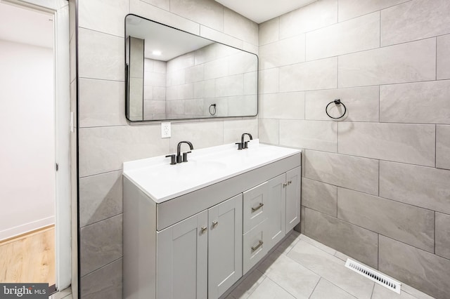 bathroom featuring double vanity, a sink, visible vents, and tile walls