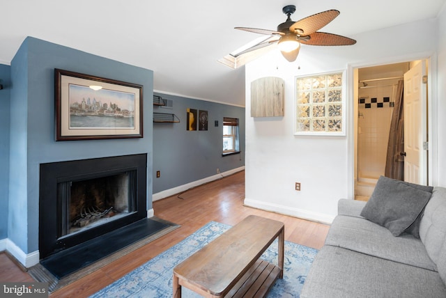 living area featuring a ceiling fan, a fireplace, baseboards, and wood finished floors