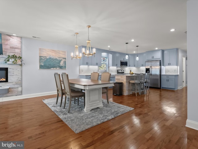 dining space with baseboards, dark wood finished floors, recessed lighting, a large fireplace, and a chandelier