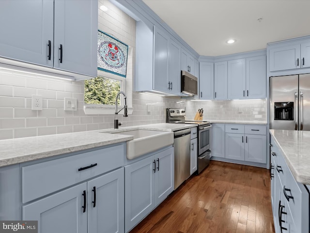 kitchen featuring a sink, appliances with stainless steel finishes, decorative backsplash, light stone countertops, and dark wood-style flooring
