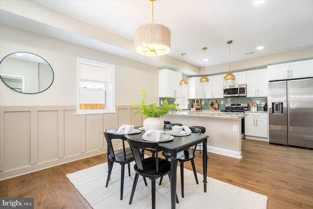 dining room featuring a wainscoted wall, light wood finished floors, a decorative wall, and recessed lighting