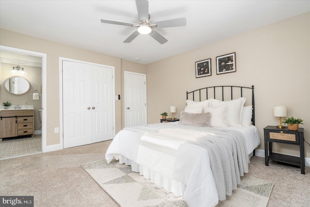 bedroom with a closet, light colored carpet, a ceiling fan, ensuite bath, and baseboards