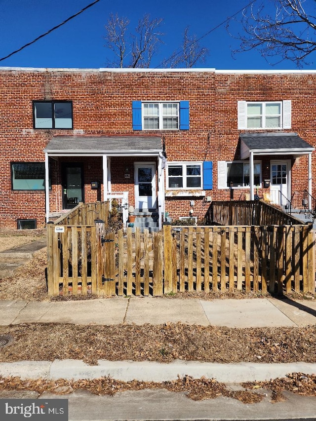 townhome / multi-family property with brick siding, a porch, and a fenced front yard