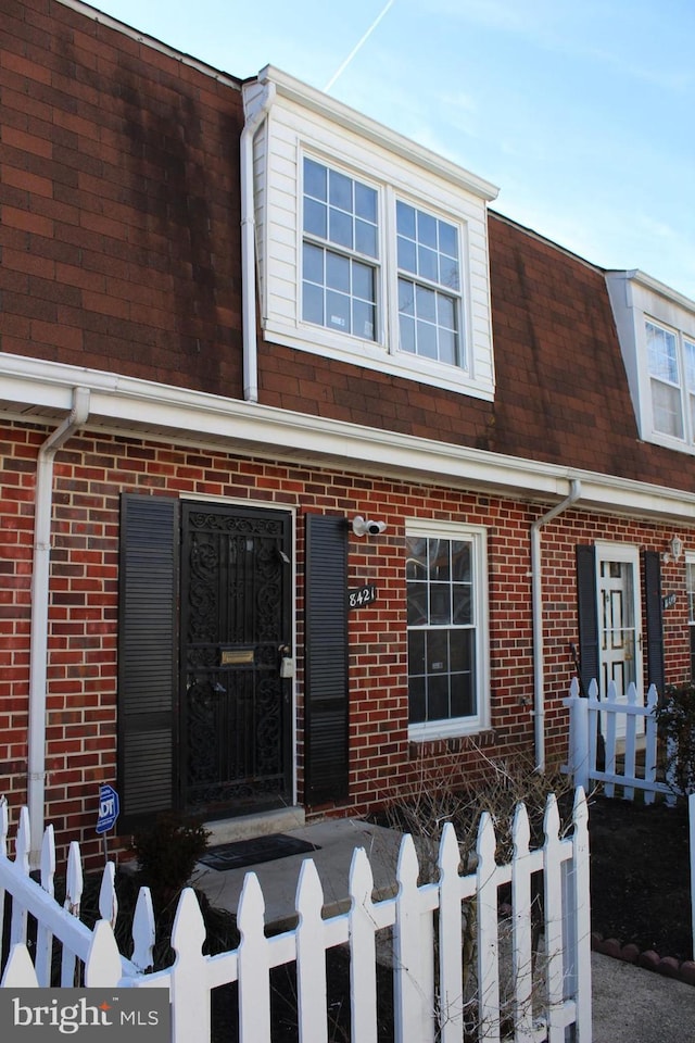 view of front of property with a fenced front yard, brick siding, and roof with shingles