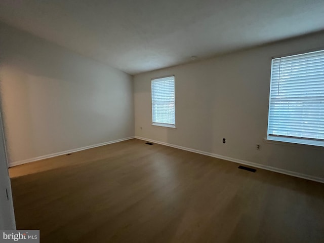 empty room with baseboards, visible vents, and wood finished floors