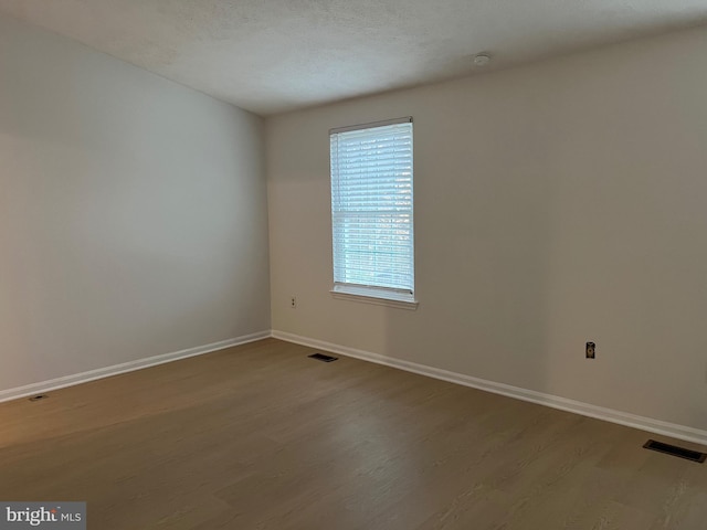 spare room featuring a textured ceiling, wood finished floors, visible vents, and baseboards