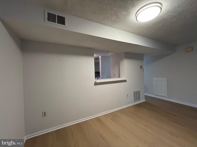 finished basement featuring visible vents, a textured ceiling, baseboards, and wood finished floors