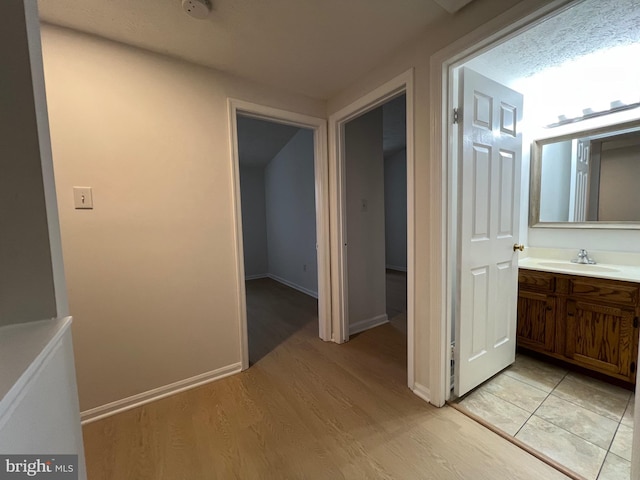 corridor with light wood-type flooring, a sink, and baseboards