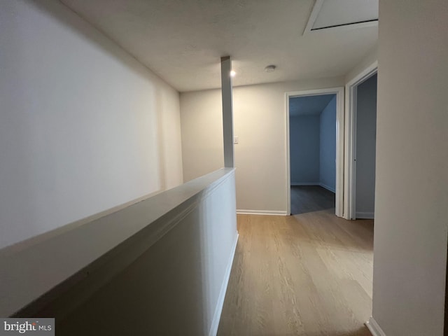 corridor with light wood-type flooring, an upstairs landing, and baseboards