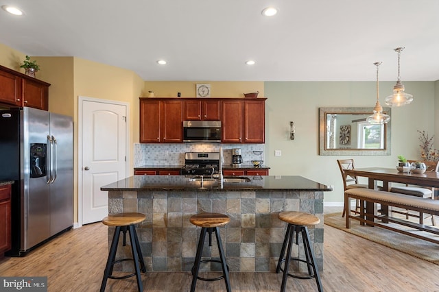 kitchen with light wood finished floors, hanging light fixtures, decorative backsplash, appliances with stainless steel finishes, and a kitchen breakfast bar