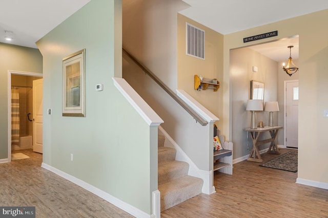 stairs featuring a notable chandelier, baseboards, visible vents, and wood finished floors