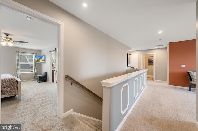 corridor with baseboards, a barn door, an upstairs landing, and light colored carpet