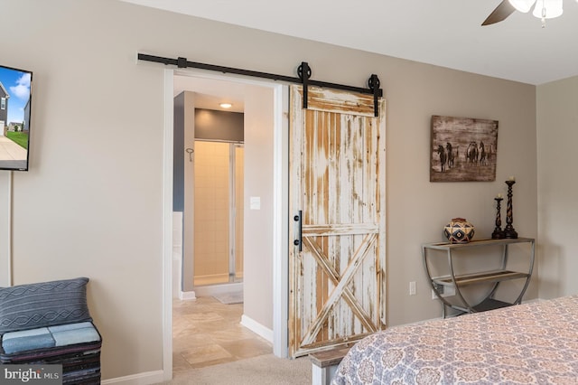 bedroom with ceiling fan, a barn door, and baseboards