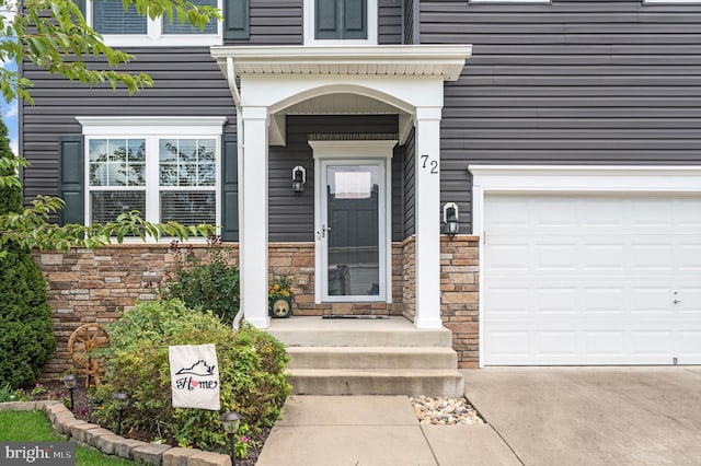 doorway to property with a garage, stone siding, and concrete driveway