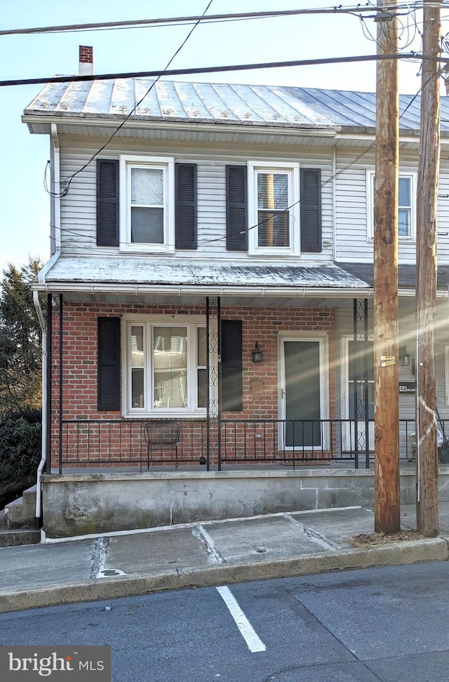 view of property featuring a porch, brick siding, and a chimney