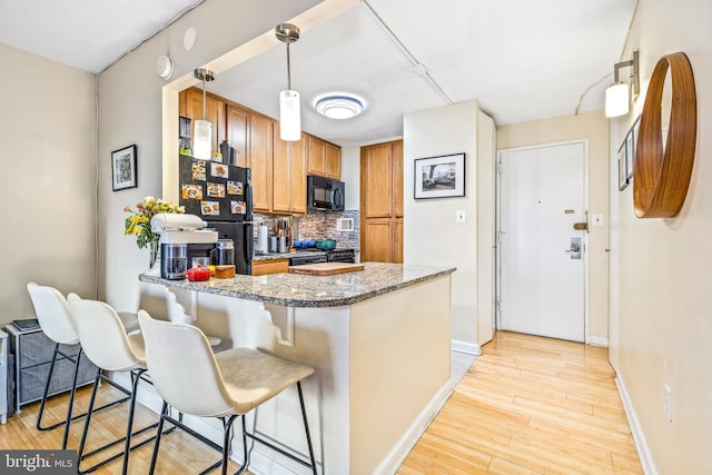 kitchen featuring a peninsula, hanging light fixtures, black appliances, brown cabinetry, and dark stone countertops