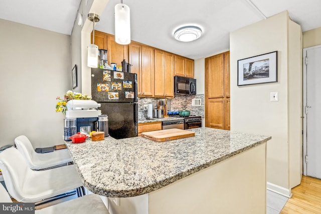 kitchen with decorative backsplash, a breakfast bar area, brown cabinets, decorative light fixtures, and black appliances