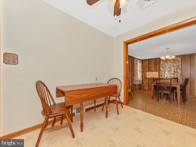 dining space with baseboards, visible vents, light floors, wood walls, and ceiling fan with notable chandelier