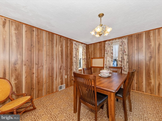 dining area with visible vents, wood walls, a notable chandelier, and a textured ceiling