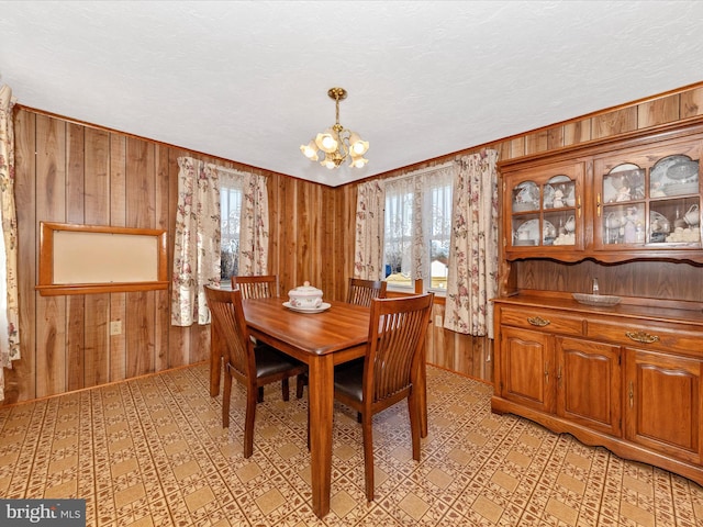 dining space featuring wood walls, a notable chandelier, a textured ceiling, and a wealth of natural light