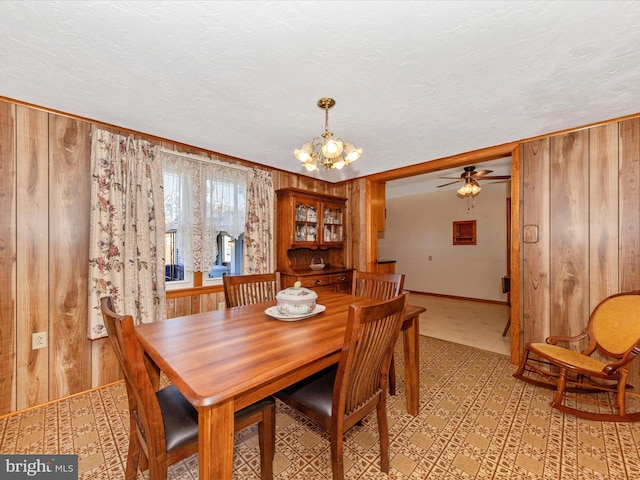 dining room featuring wood walls, baseboards, a textured ceiling, and an inviting chandelier