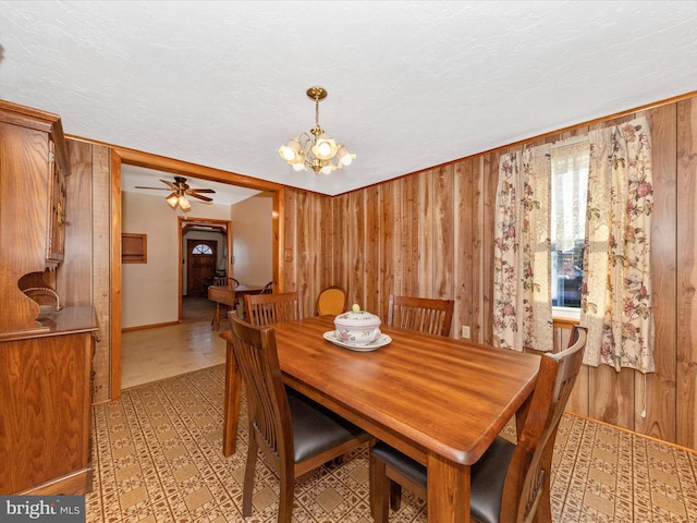 dining area featuring a textured ceiling, wood walls, and ceiling fan with notable chandelier