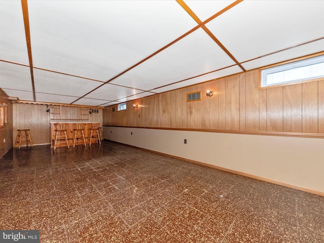 below grade area with a dry bar, visible vents, wood walls, baseboards, and tile patterned floors