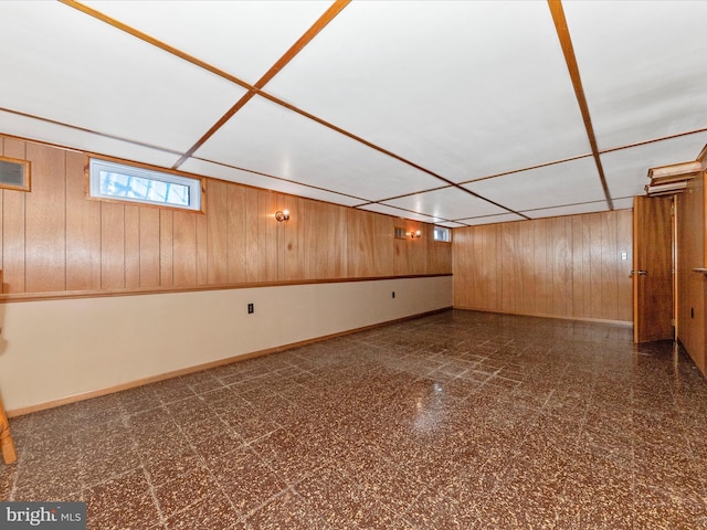 below grade area with dark floors, wood walls, a drop ceiling, and baseboards